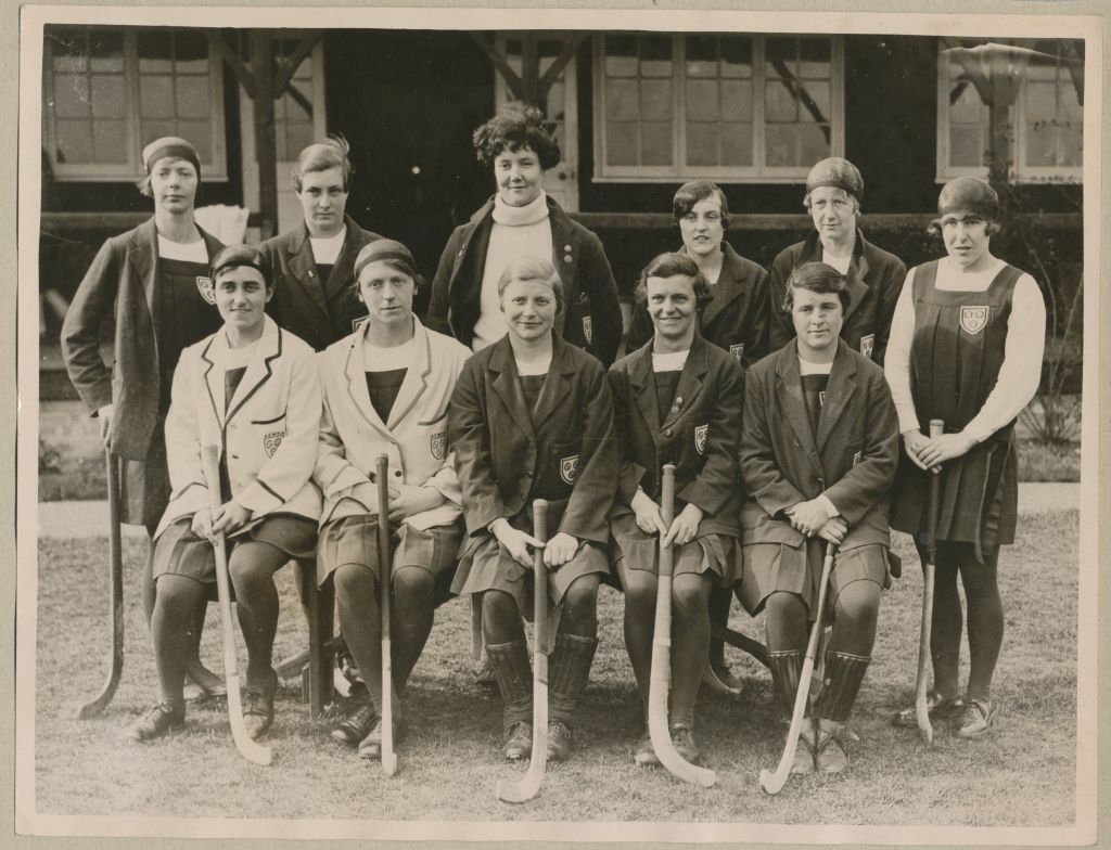 Black and white photographic group portrait of members of the England women’s hockey team, including D. Northwood and V. Chamberlain (front row right), 1927.